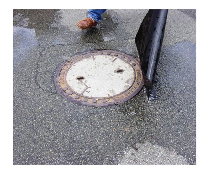 Plaque d'obturation carrée noire à usage unique 80cm x 80cm positionnée sur un regard d'égout.